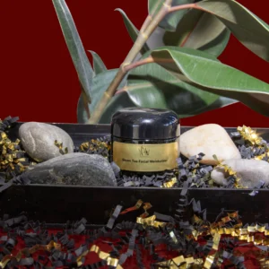 A jar of cream among stones, leaves, and a red background.
