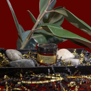 A jar of honey surrounded by stones, leaves, and decorative gold accents on a red background.