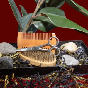 A hairbrush and scissors resting on a natural surface with leaves in the background.