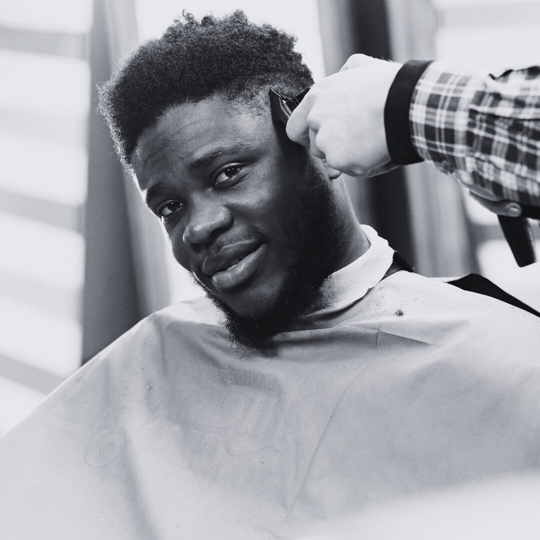 A man getting a haircut, smiling as the barber works.